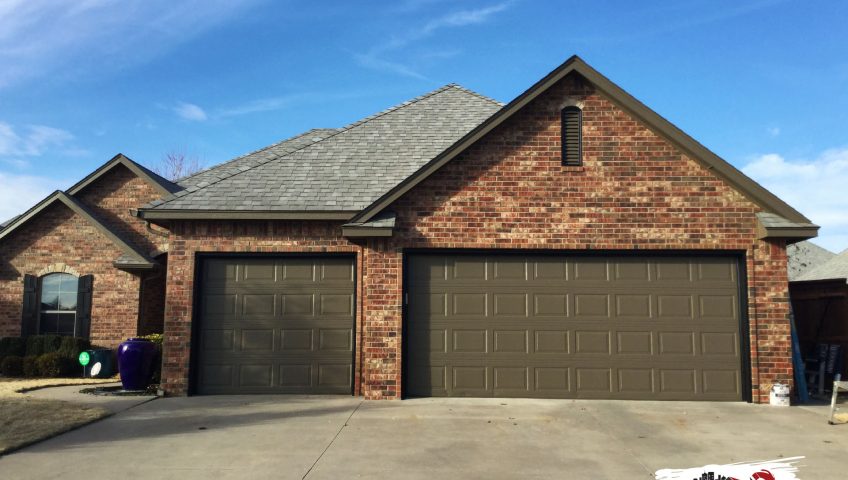 a newly painted brown garage attached to a brick house in oklahoma