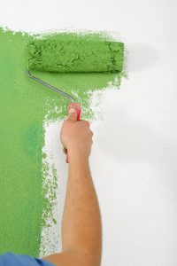 painter using a roller to paint a wall green
